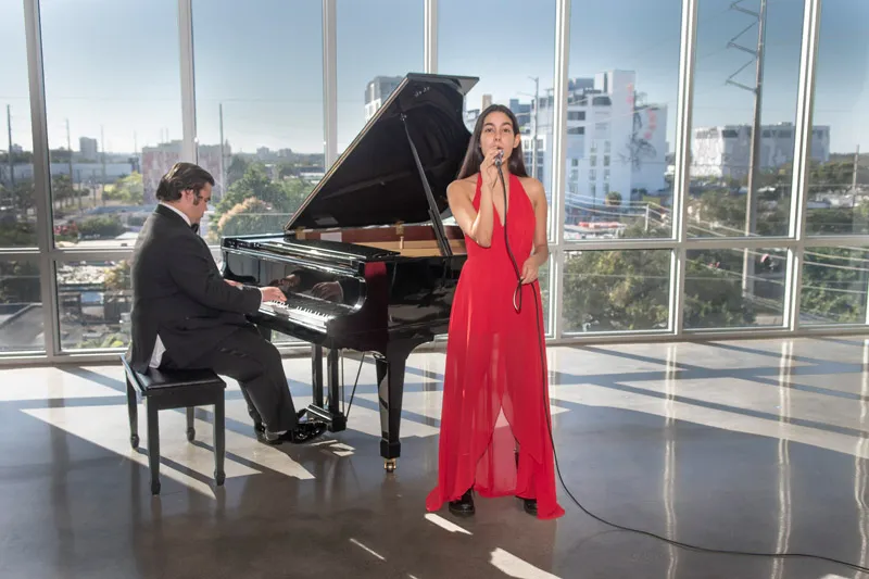 Female student sining while a male student is playing a piano